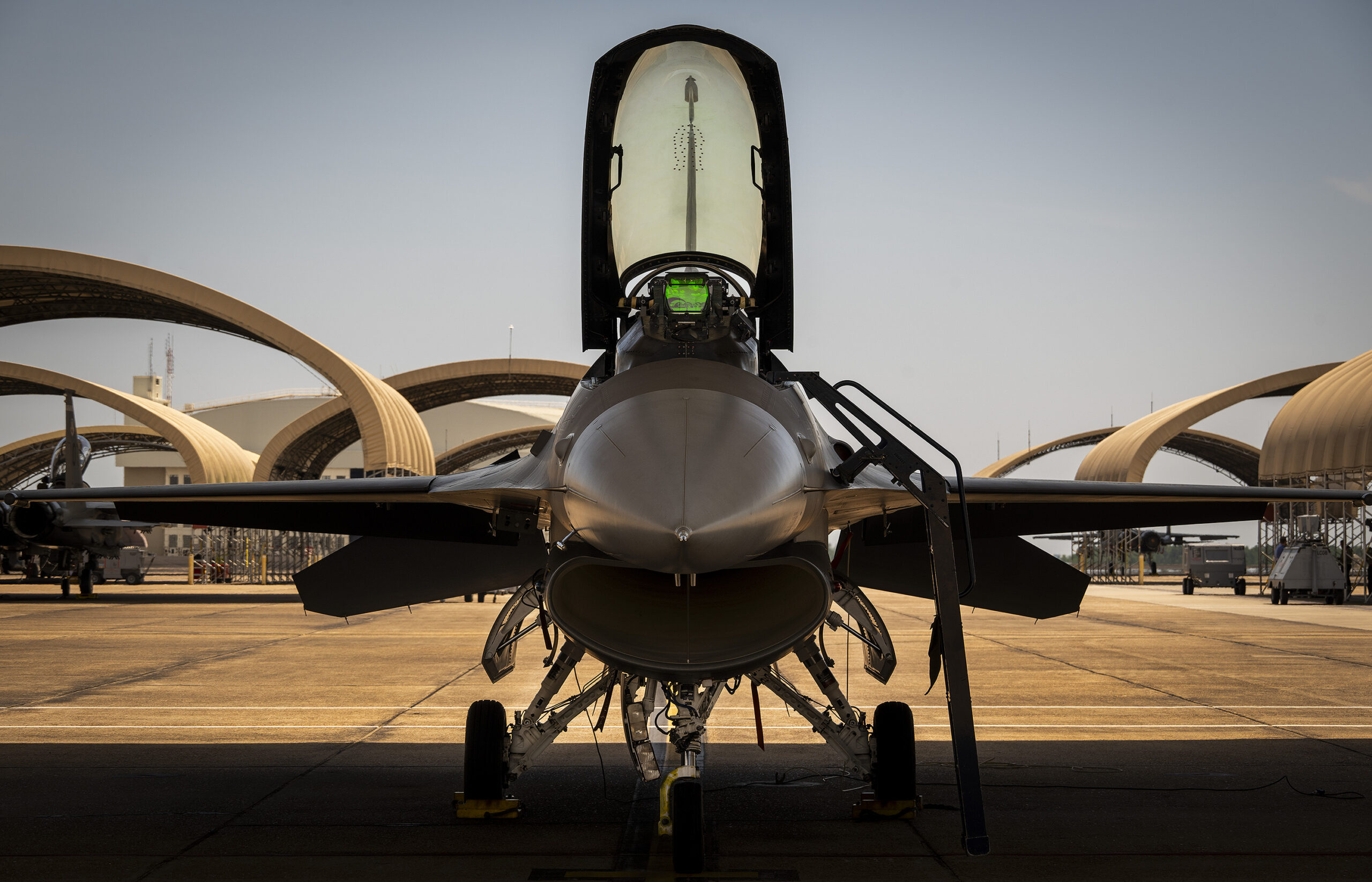 F-16 aircraft faces the viewer with cockpit open. There is a visibly green heads up display operating under the opened canopy.